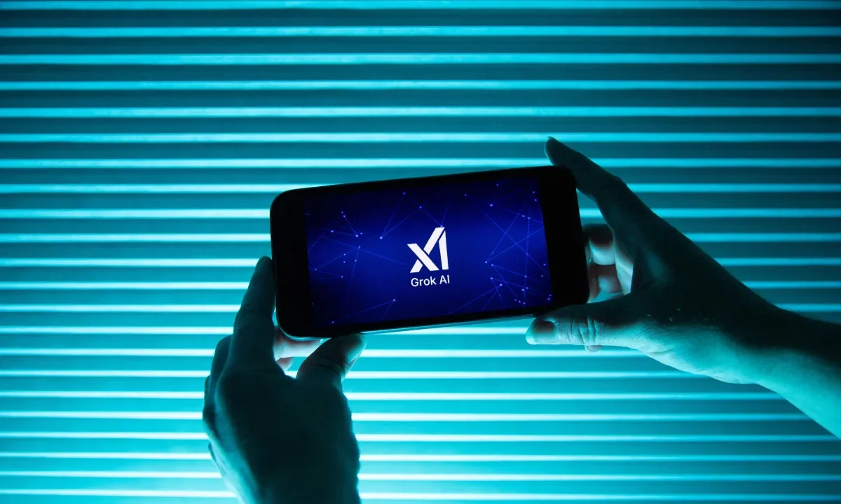 A person holds a telephone displaying the logo of Elon Musk s artificial intelligence grok in front of a background lit by a blue light.