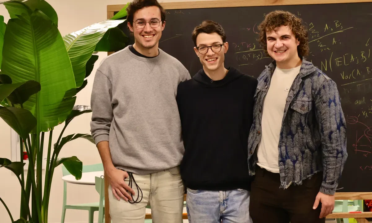 Three smiling men stand in front of a chalkboard