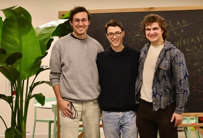 Three smiling men stand in front of a chalkboard