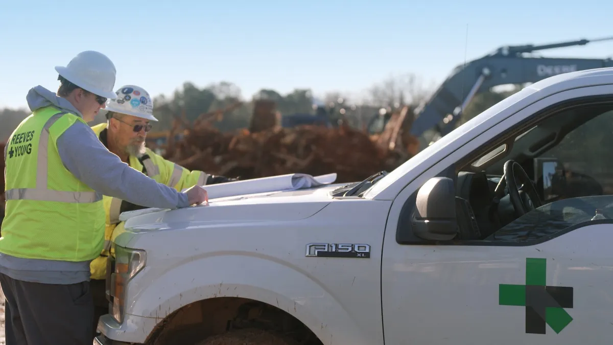 Two workmen look at plans on the hood of a Ford F150