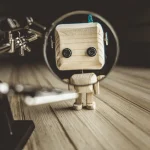 Wooden Robot Android Stands On A Table Under A Magnifying Glass. Metal Clamps With Magnifying Glass