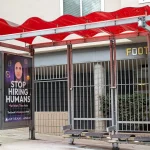 Bus stop shelter with red canopy and ad for Artisan AI reading "Stop Hiring Humans" and "For Work They Hate" on city sidewalk, San Francisco, California, September 30, 2025. (Photo by Smith Collection/Gado/Getty Images)