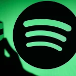 The Spotify logo displays on a screen with a person holding a phone.