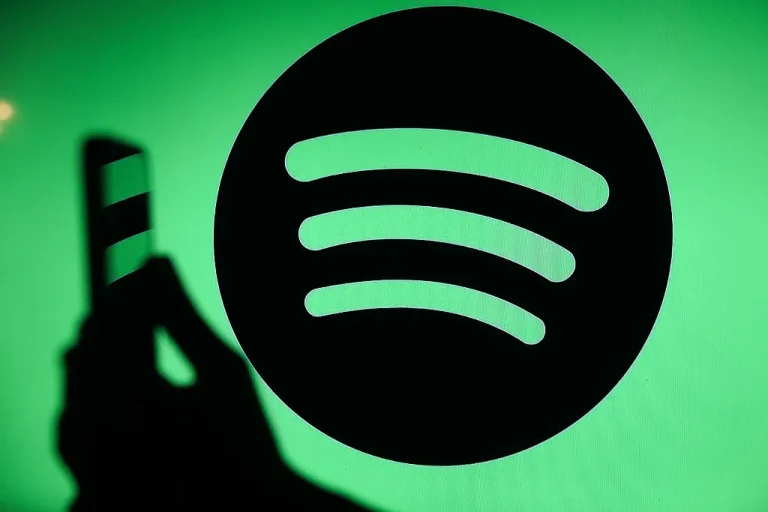 The Spotify logo displays on a screen with a person holding a phone.