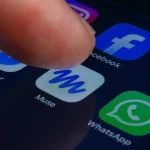 A close-up of a human finger pressing the Muse app icon inside a folder containing Meta apps on a smartphone screen.