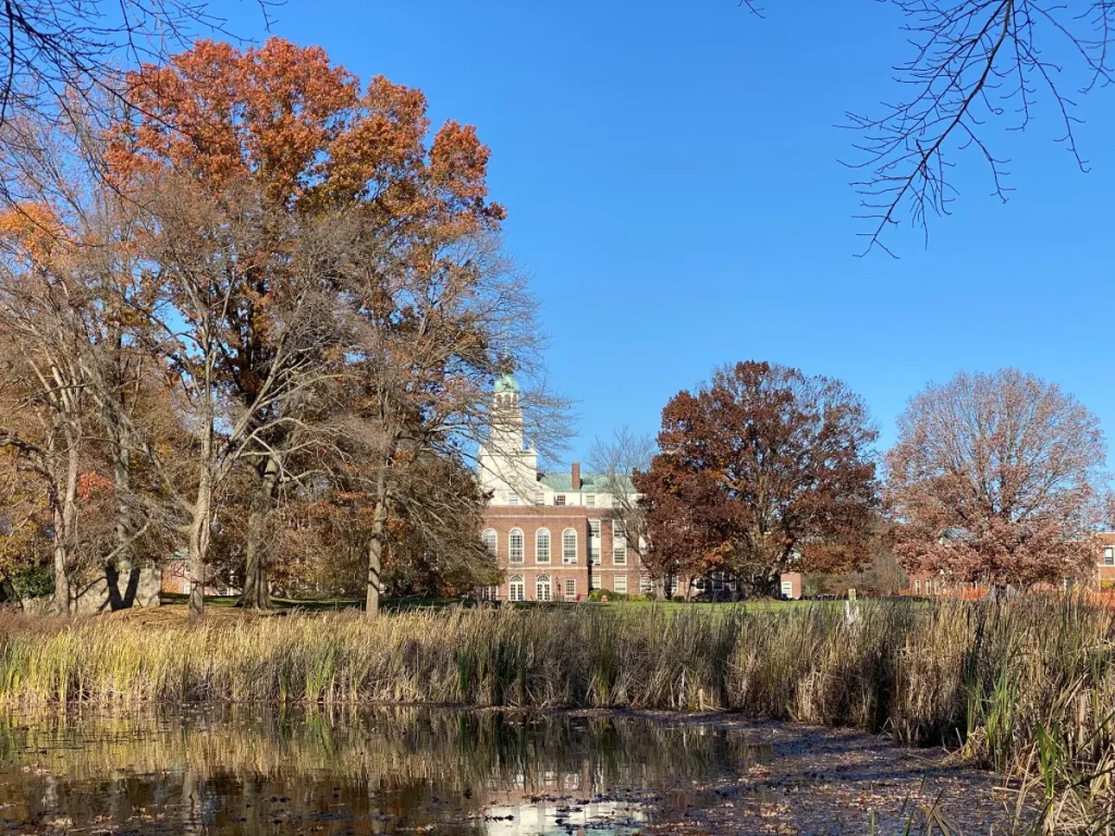 A wooded lake, with a stately Georgian brick building visible in the distance.