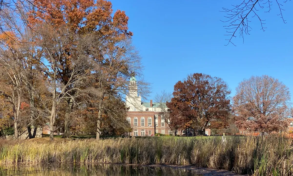 A wooded lake, with a stately Georgian brick building visible in the distance.