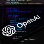 The OpenAI logo is displayed on a smartphone screen placed on a reflective surface onto which lines of computer code.