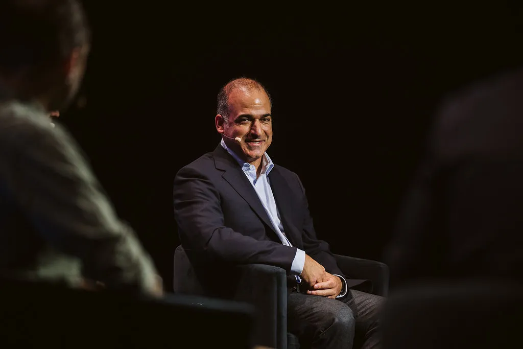 A man in a business suit sits on a conference stage