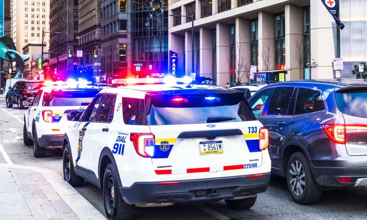 Police vehicles with their lights flashing alongside traffic in downtown Philadelphia.
