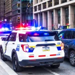 Police vehicles with their lights flashing alongside traffic in downtown Philadelphia.