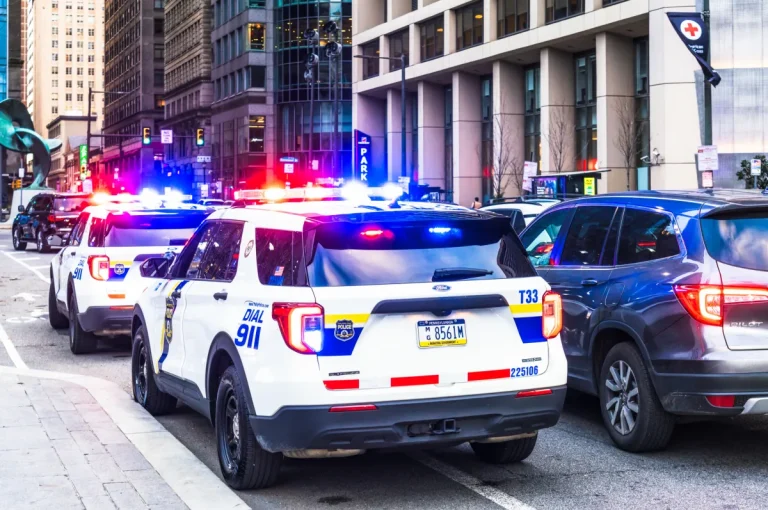 Police vehicles with their lights flashing alongside traffic in downtown Philadelphia.